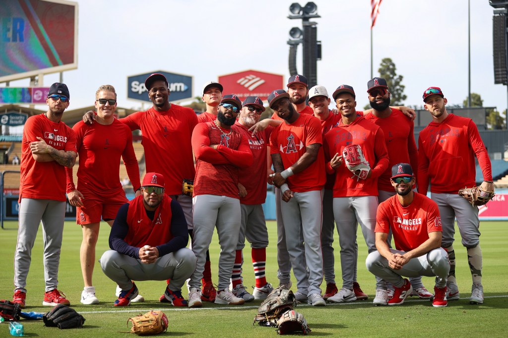 Baseball players in red shirts with "Angels Baseball" printed on them pose together on a baseball field.