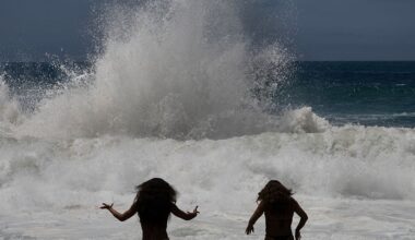 a silhouette of two young women is seen against the splashing of an ocean wave