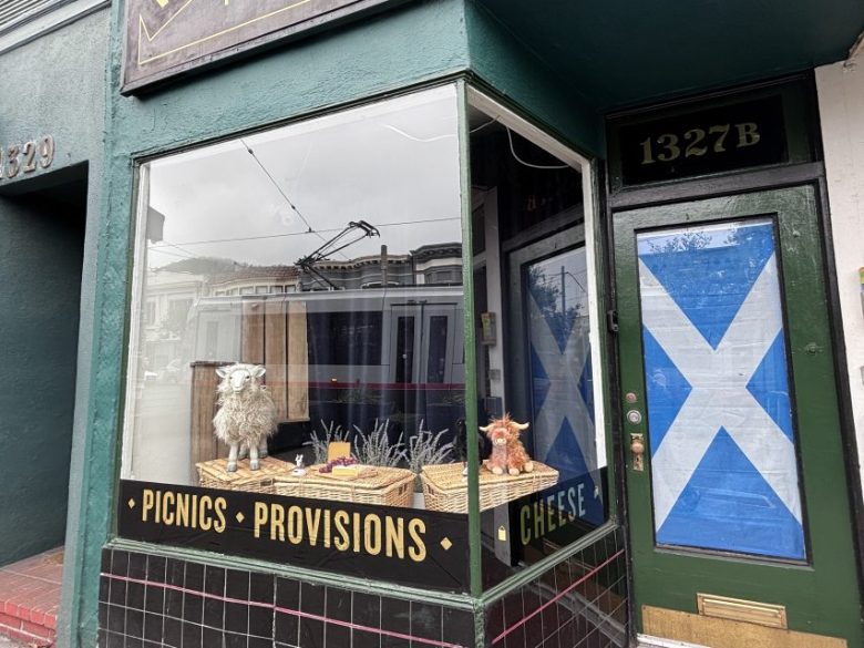 Storefront with "Picnics Provisions Cheese" signage, Scottish flag on the door, and animal plush toys displayed in the window. Address 1327B is visible above the door.