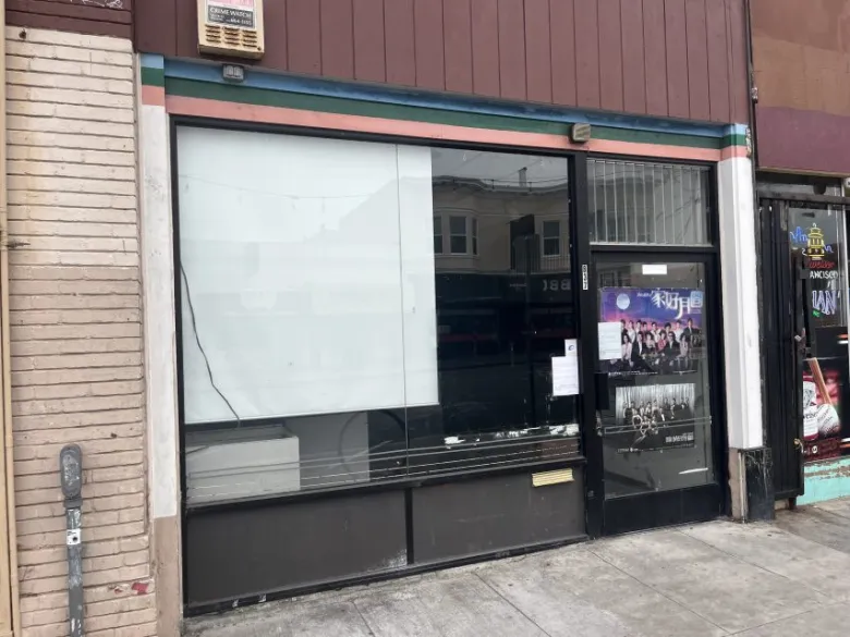 A storefront with large windows, partially covered with white paper. There is a paper notice on the glass door and a parking meter on the sidewalk in front.