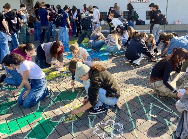 High school students kneel to paint a mural on a brick street