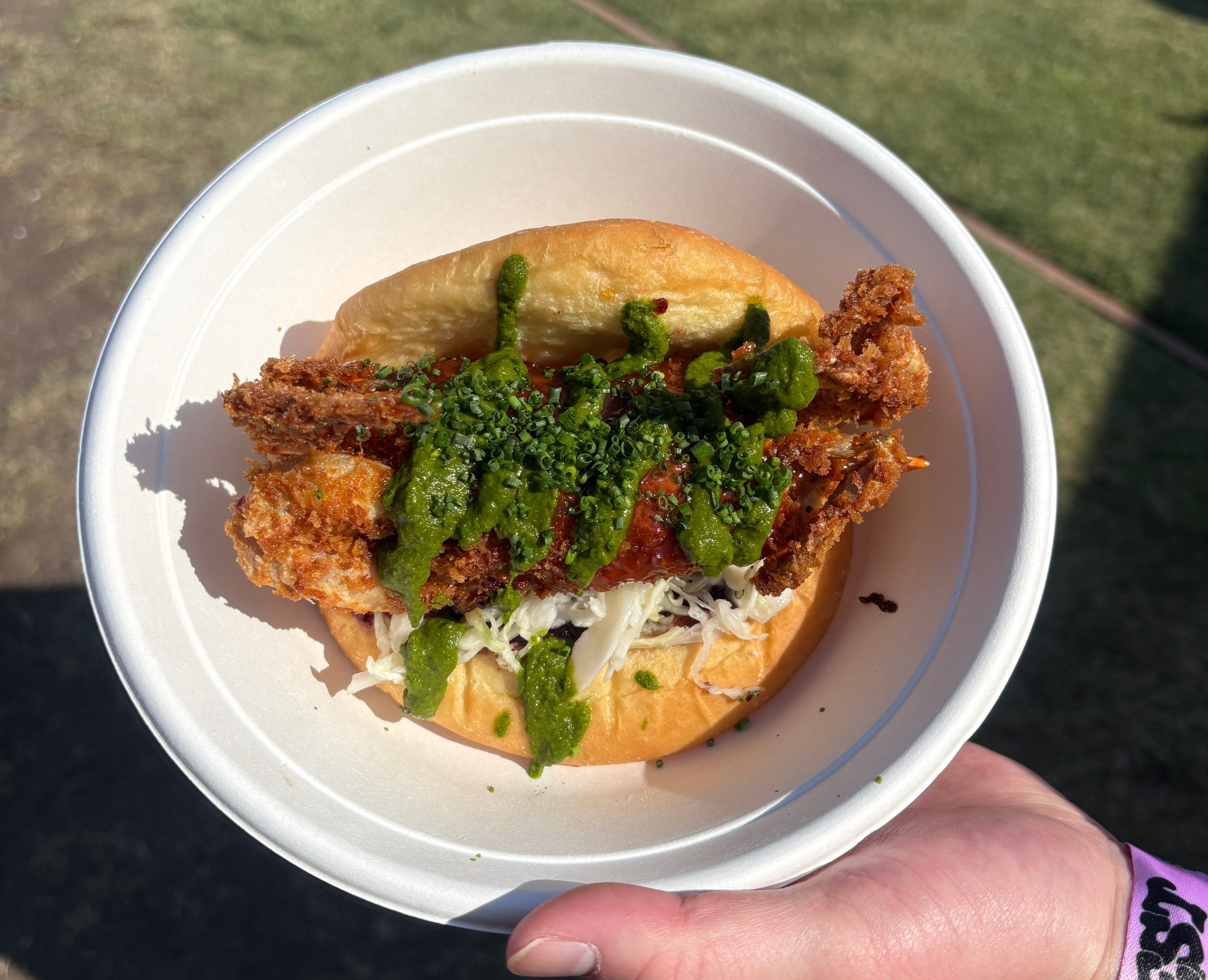soft shell crab sandwich drizzled with green sauce in a white bowl