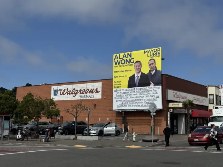 A Walgreens Pharmacy building with a large campaign billboard for Alan Wong and Mayor Lurie displayed in the parking lot. People and cars are visible in front of the store.