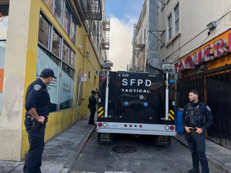 SFPD tactical vehicle parked in a narrow alley with three uniformed officers standing nearby; buildings and a taqueria are visible.