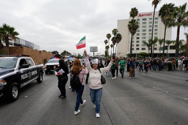 Fans wave flags as the Iran World Cup soccer team leaves their hotel for the airport Tuesday, June 30, 2026, in Tijuana, Mexico. (AP Photo/Gregory Bull)