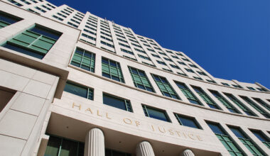 Exterior of a Hall of Justice building, viewed from below against a clear blue sky.