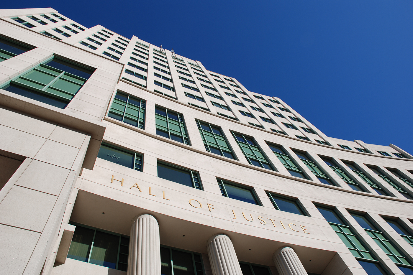 Exterior of a Hall of Justice building, viewed from below against a clear blue sky.