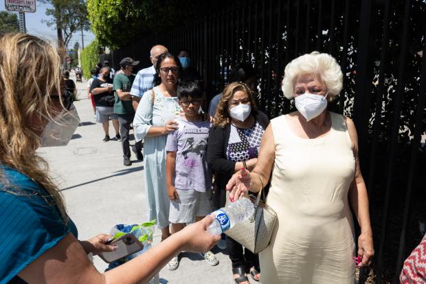 From left, volunteer Lorena Bautista hands Rosa Chambers a bottle of water during an event hosted by Via Care Community Health Center to support residents affected by the Boyle Heights warehouse fire in Los Angeles on Tuesday, June 23, 2026. (Photo by Drew A. Kelley, Press-Telegram/SCNG)