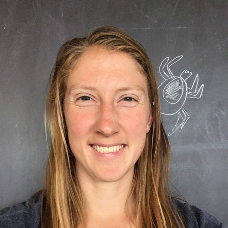 Headshot of Lisa Couper with a tick drawn on the blackboard behind her