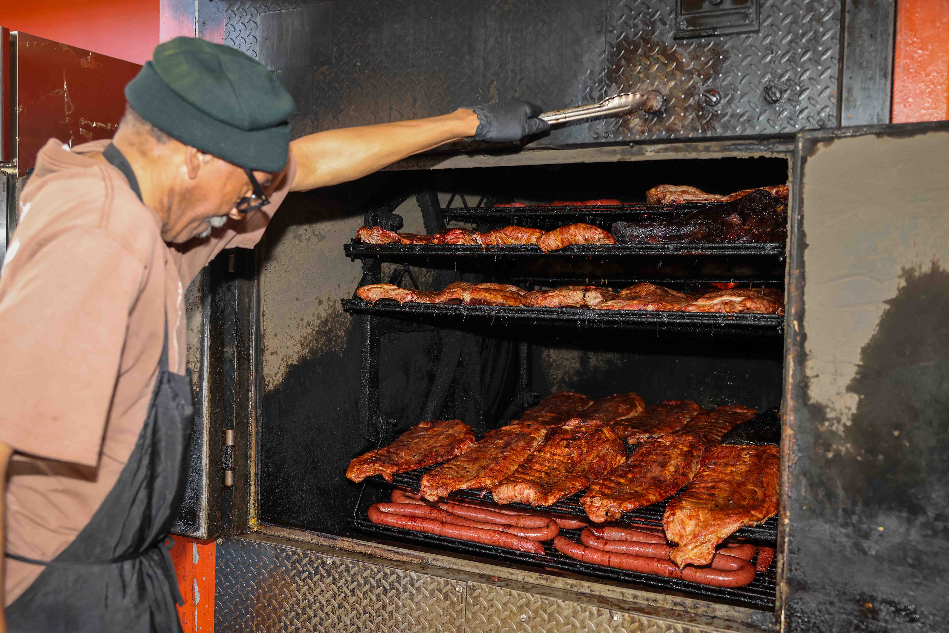 Cook Henry Rhodes checks the ribs, chicken, sausage and other...