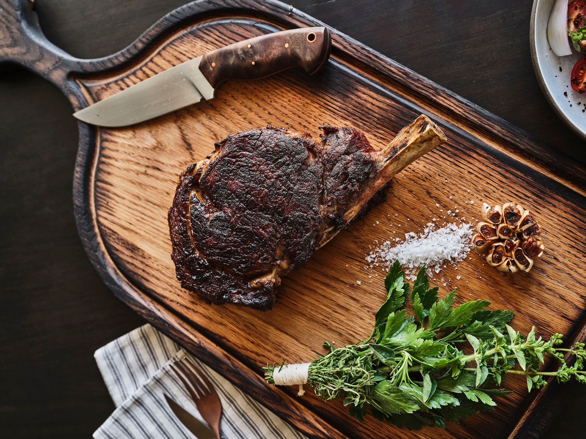 An overhead shot of a well seared steak with chunky knife on a wooden cutting board at Mattei’s Tavern.