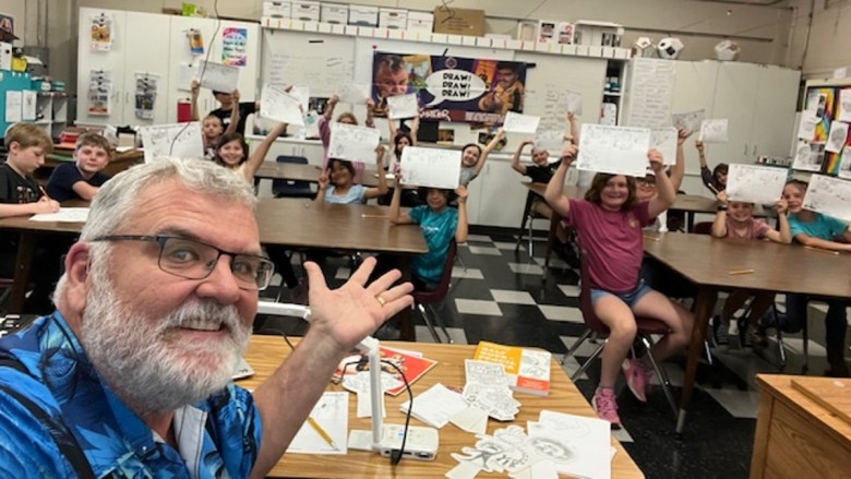 A teacher's selfie with students holding up sheets of paper filled with their drawings