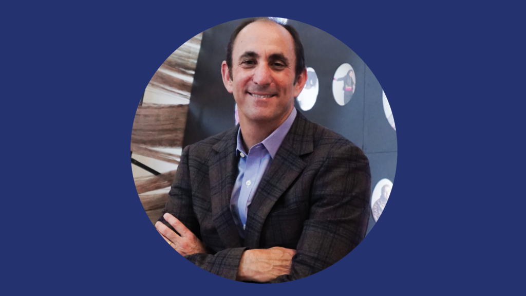 Portrait of Micah Parzen wearing a suit jacket and blue-collared shirt with his arms crossed.