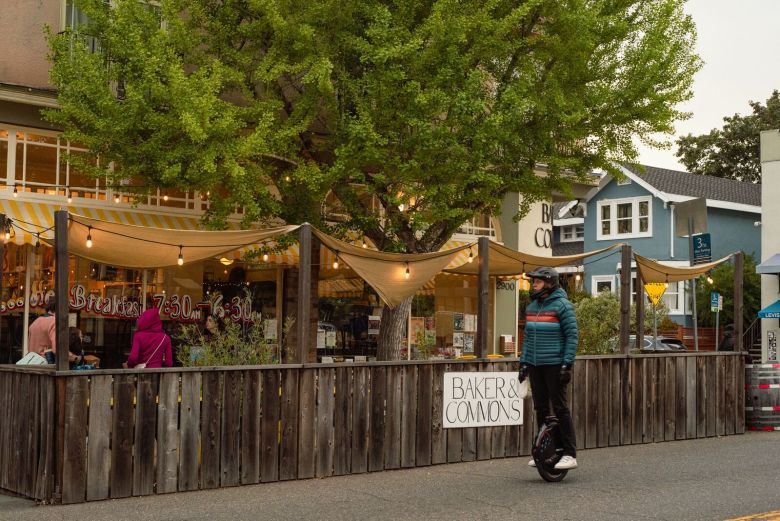 A person rides past the attractive parklet for the restaurant Baker and Commons, which is decorated with string lights and shades