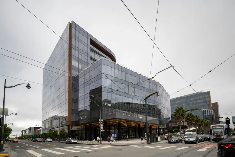 panoramic photo of a glass-walled building bearing the word "Uber" on a busy street corner