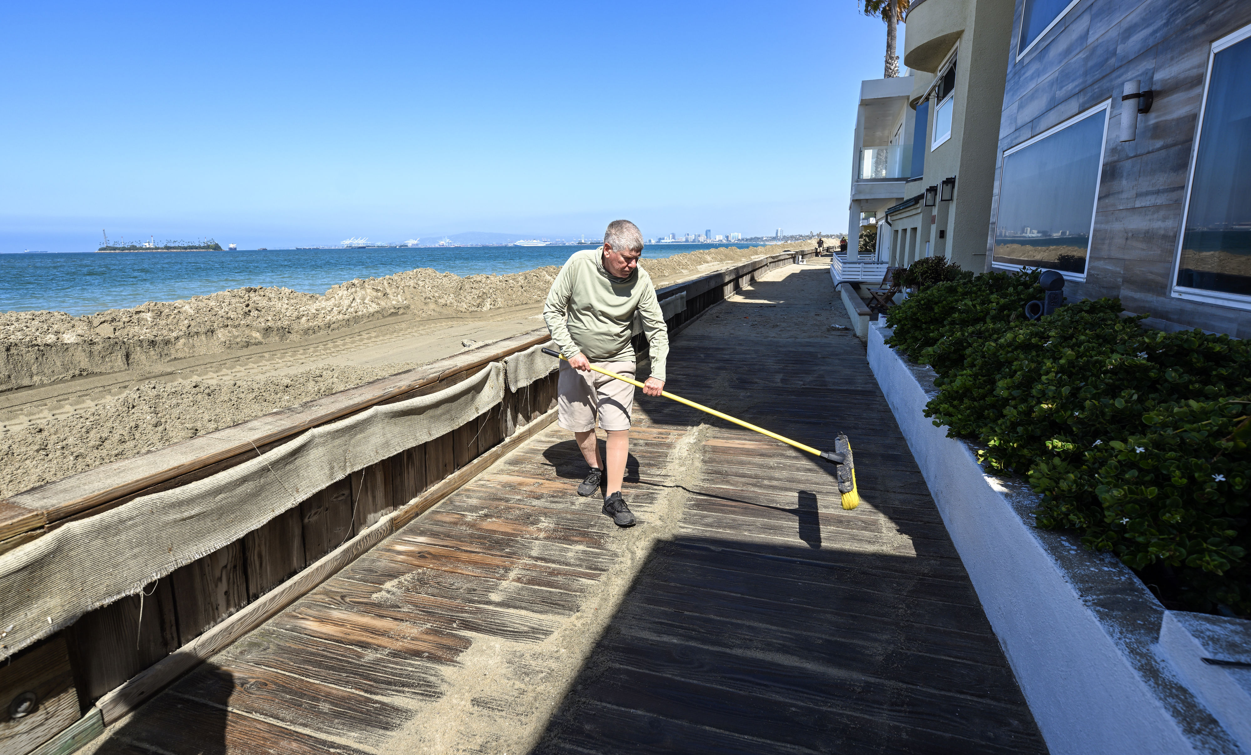 Ken Holt cleans up sand along the boardwalk in front...