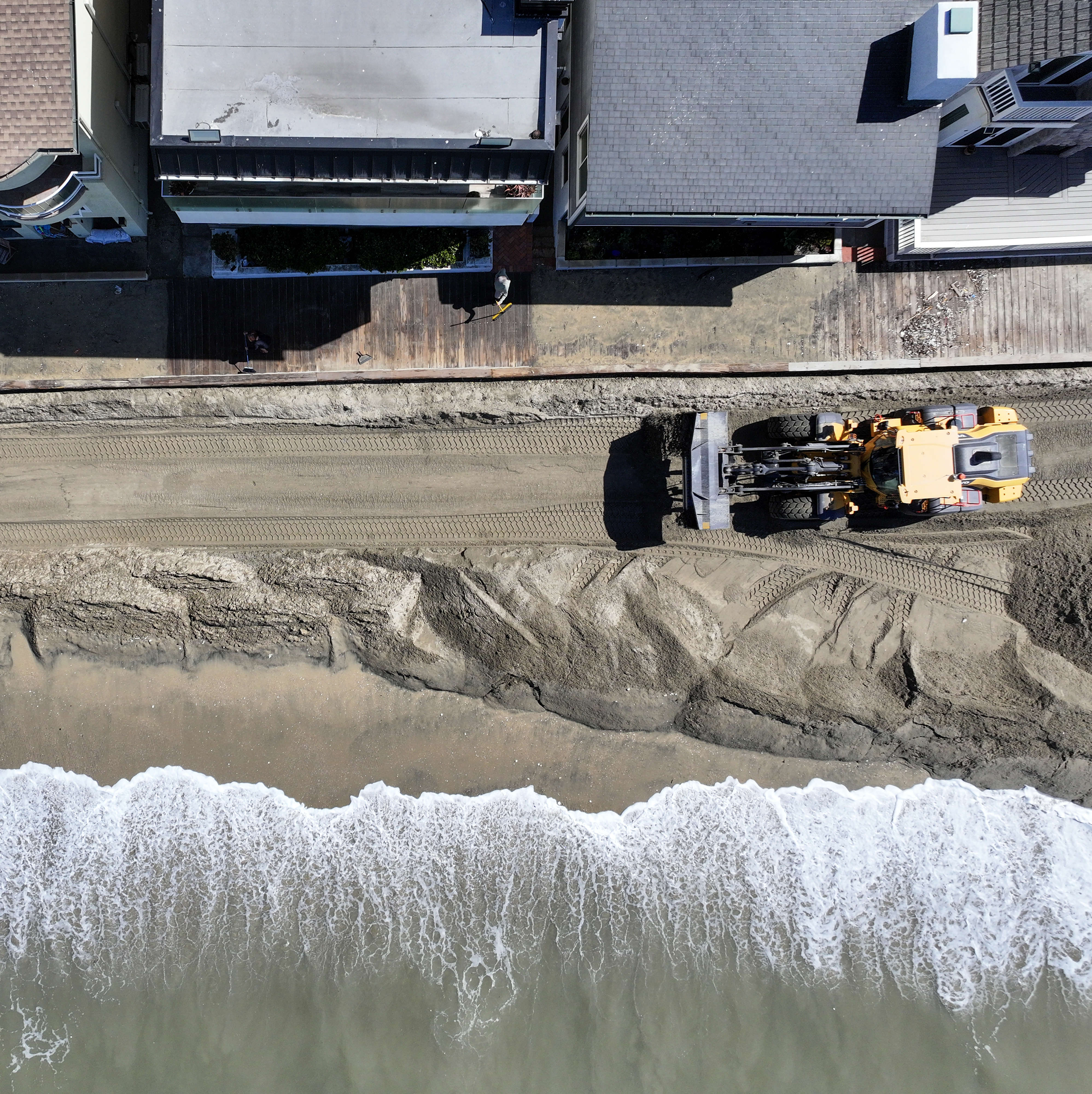 Ken Holt cleans up sand along the boardwalk in front...