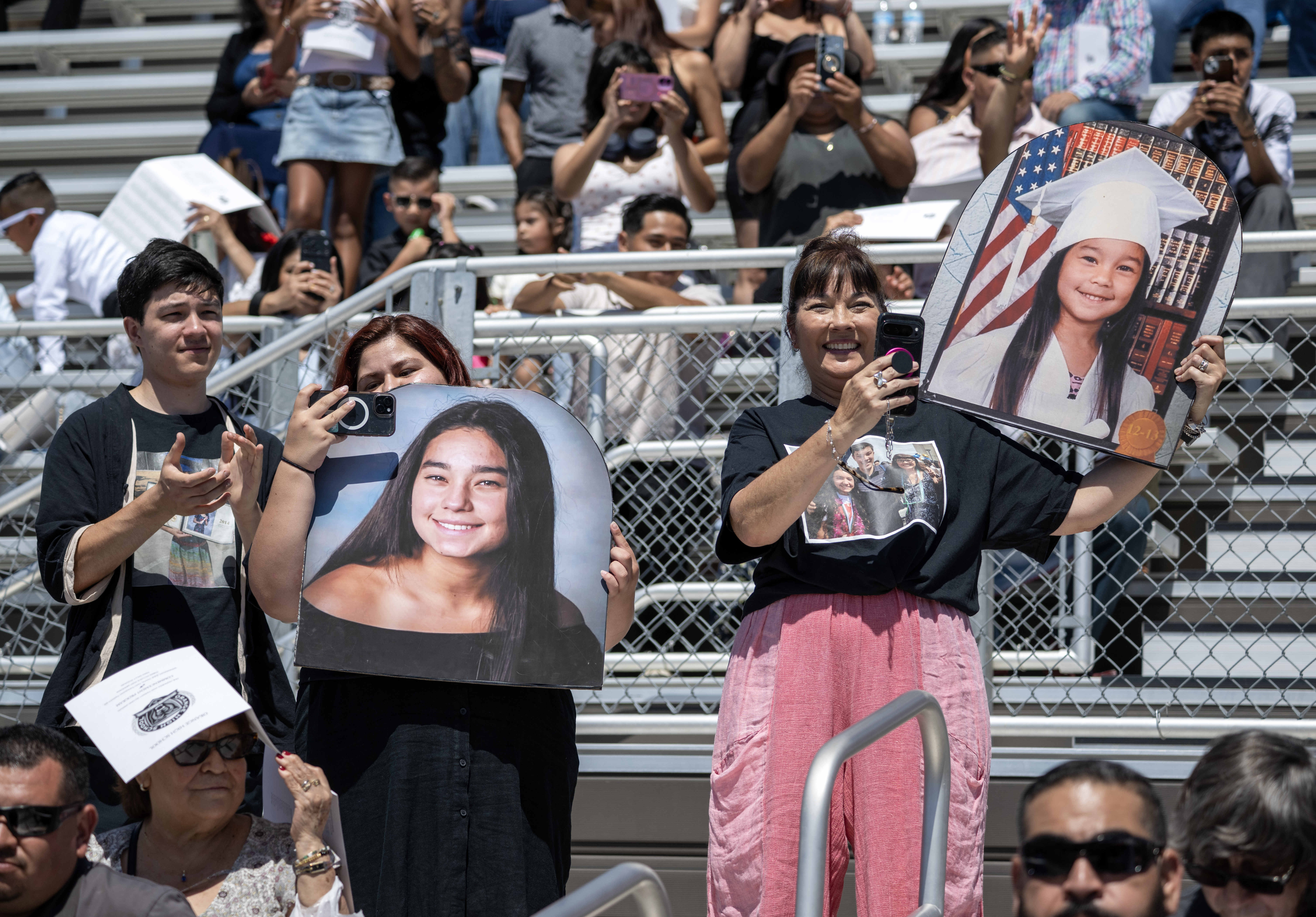 Proud parents hold up enlarged photos of their kids as...