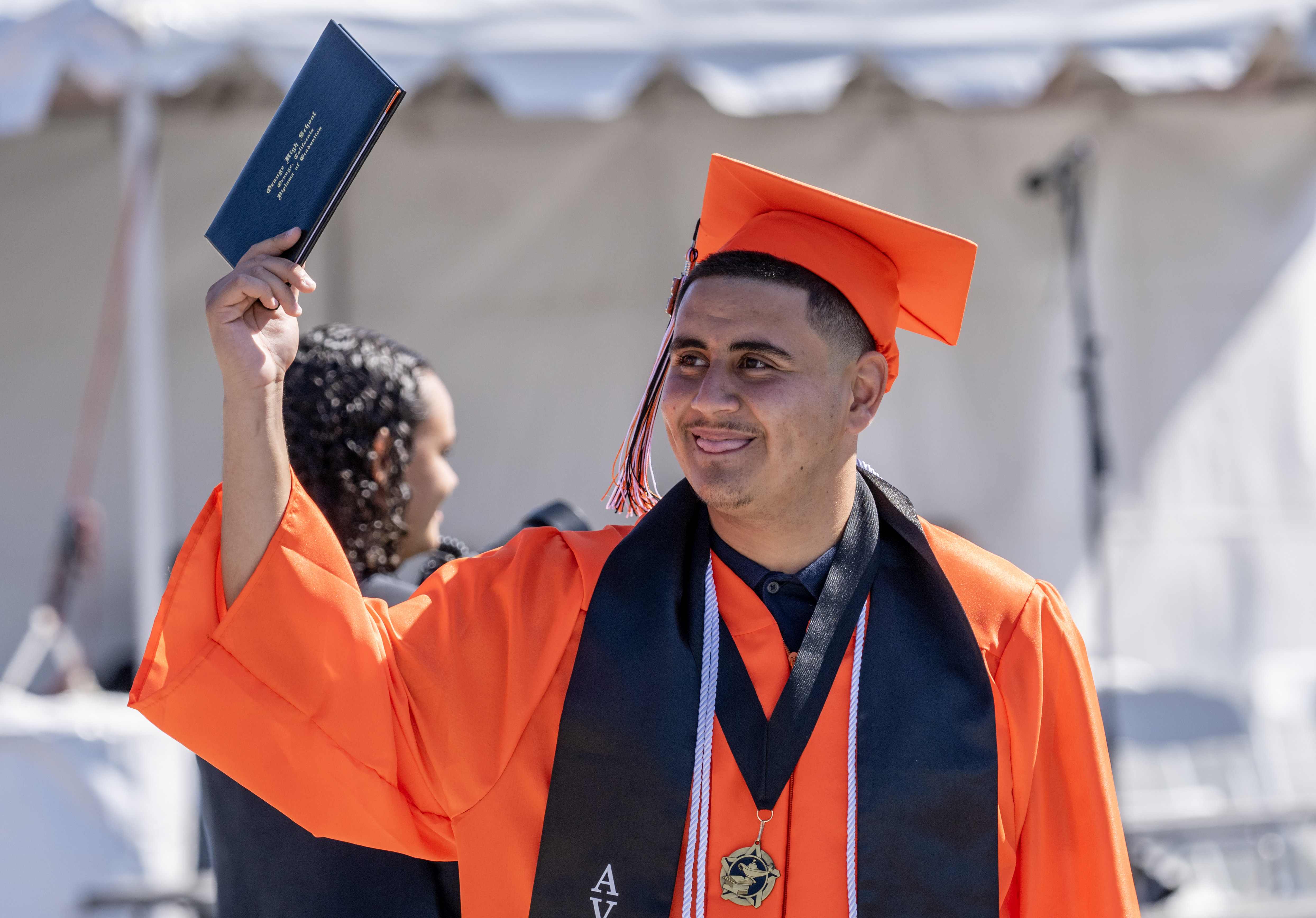 Jorge Godinez holds up his new diploma toward his loved...