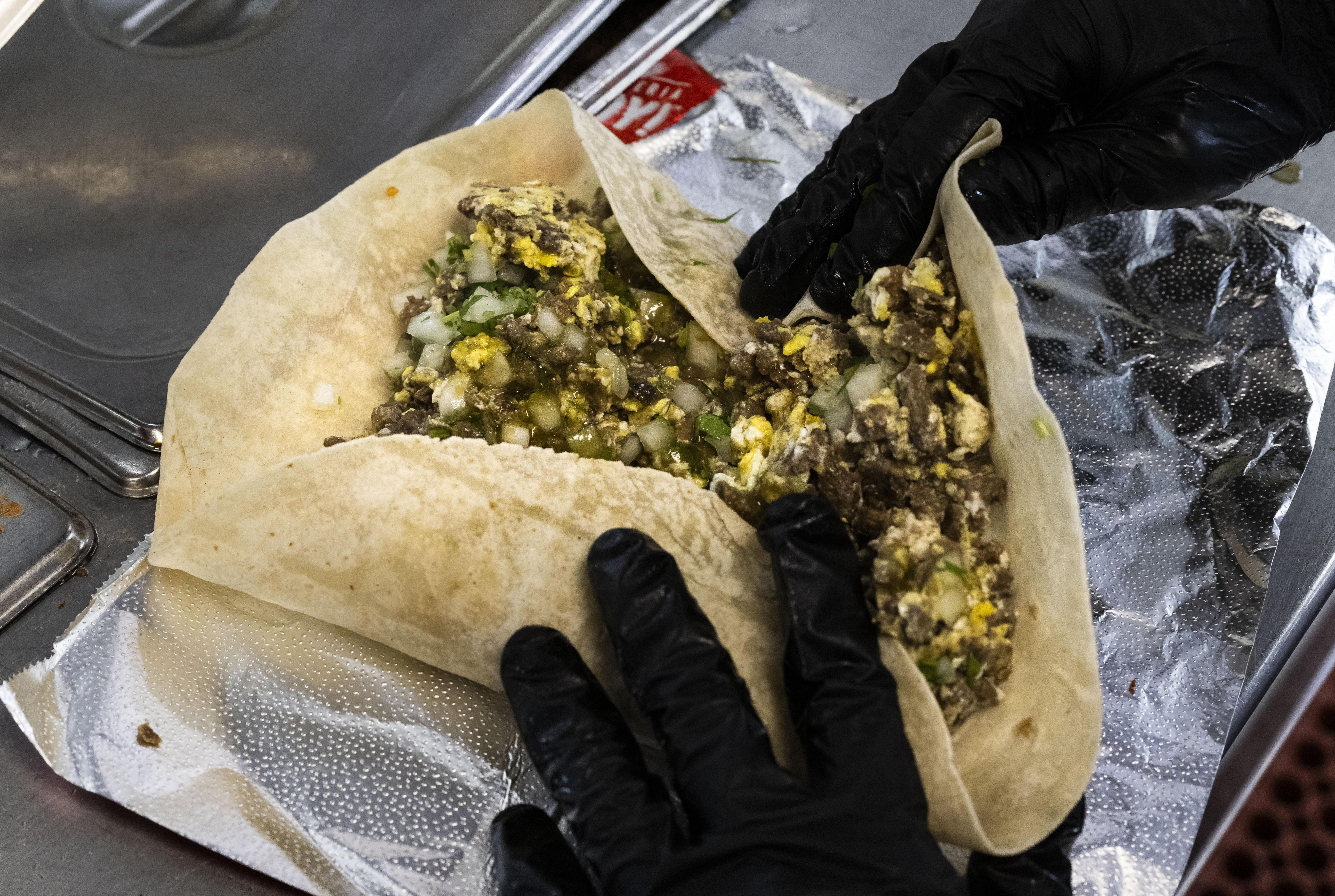 A cook makes a steak and egg burrito at Taqueria...