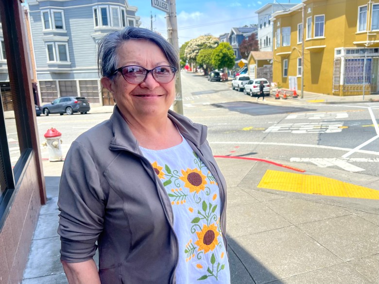 Woman in sunflower shirt stands outside on sidewalk