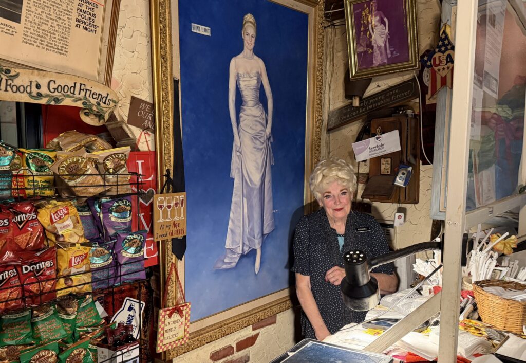 A woman standing in front of a painted self-portrait