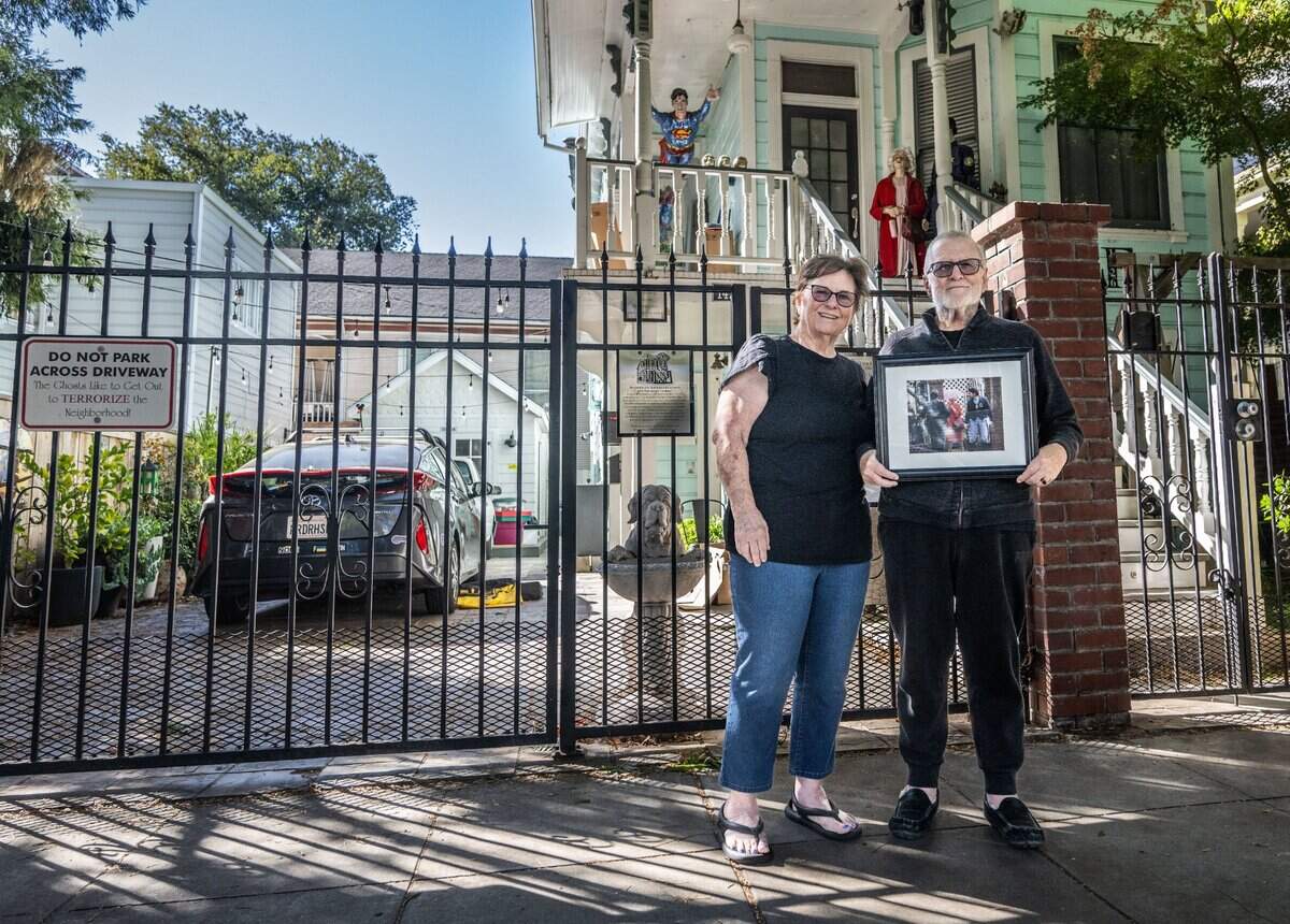 Barbara Holmes and Tom Williams, the owners of the former home of the infamous Dorothea Puente at 1426 F St. in Sacramento, pose in 2024 in front of the house with a Sacramento Bee news photograph of the late serial killer leaving the scene during the police investigation.