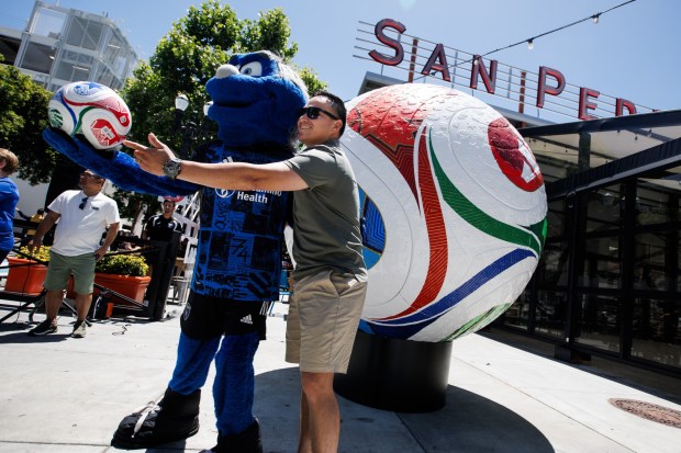Steven Urrea of San Jose poses with San Jose Earthquakes mascot, Q, for a photo in front of a large Trionda World Cup soccer ball installation outside San Pedro Square Market after a news conference on Monday, June 8, 2026, in San Jose, Calif. (Dai Sugano/Bay Area News Group)