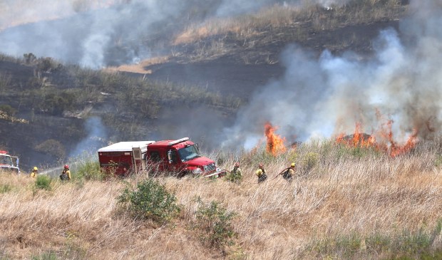 San Marcos firefighters hold fire on a ridge a quarter mile from homes on Shadow Tree Drive near Rivertree Drive in Oceanside Wednesday. (John Gastaldo / For The San Diego Union-Tribune)