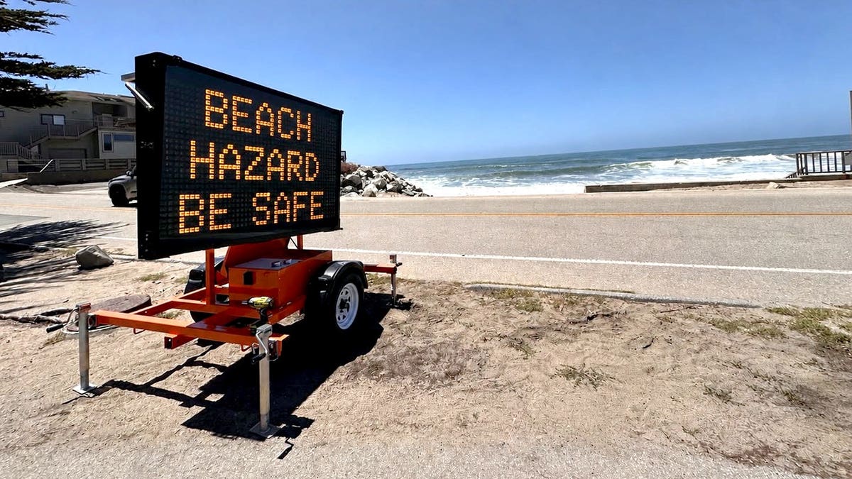 a sign warning of beach hazards along a roadway near the ocean