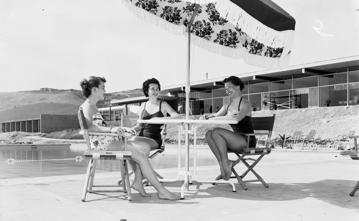 Seated at table under umbrella with pool and main public...