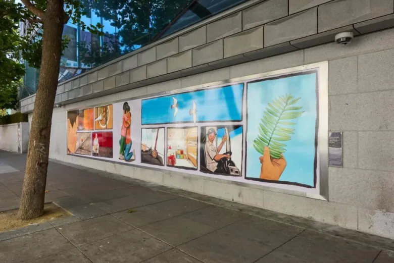A mural on a gray stone wall depicts various scenes including a woman kneeling, a driver, a hand holding a leaf, and birds flying, on a city sidewalk beside a tree.