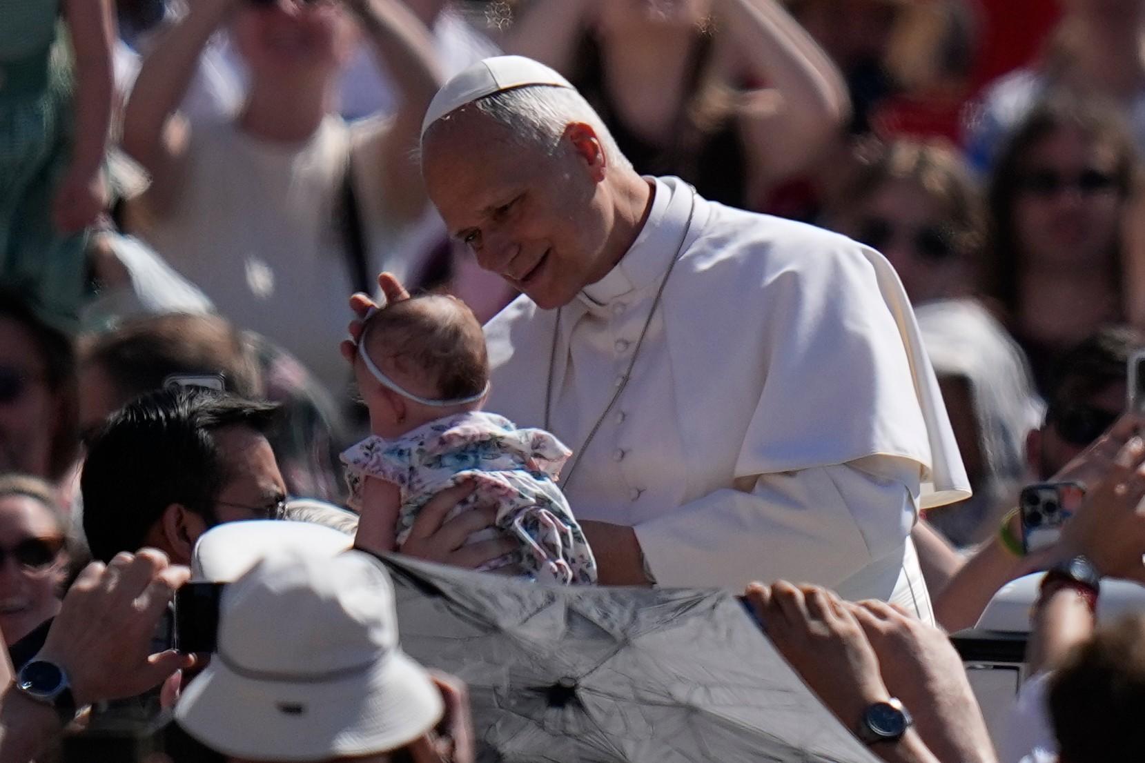 Pope Leo XIV blesses a newborn as he arrives for his weekly general audience.