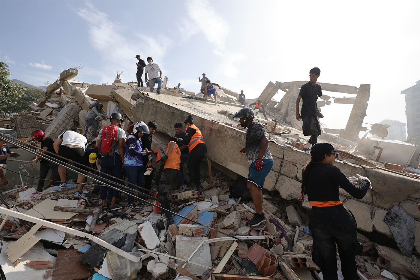 Rescue workers and civilians search through the rubble of a collapsed building following an earthquake in Venezuela.