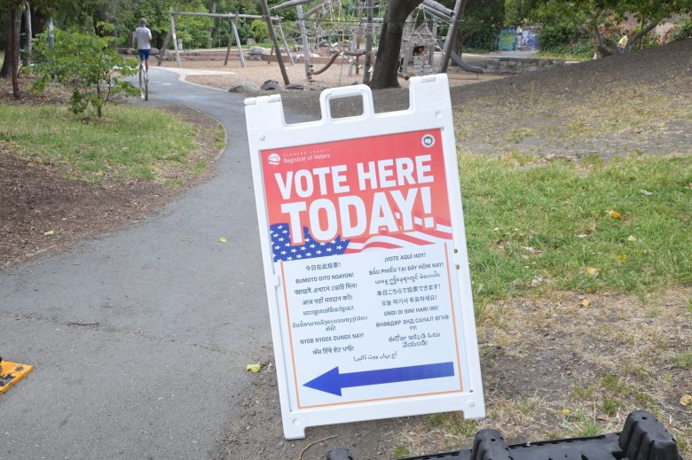 "Vote here today" sign in front of park background with playground equipment