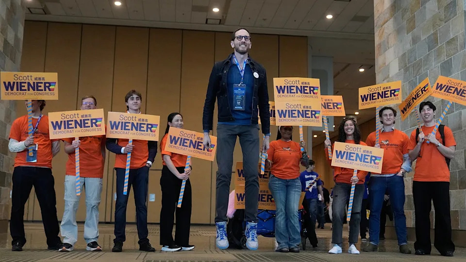 Scott Wiener jumping in the air while posing for photos with a group of people.