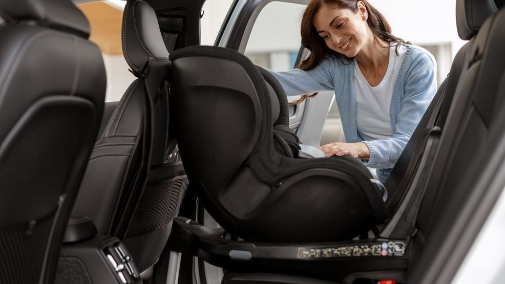 Smiling mother securing a baby car seat in a vehicle, prioritizing child safety while preparing for a family road trip