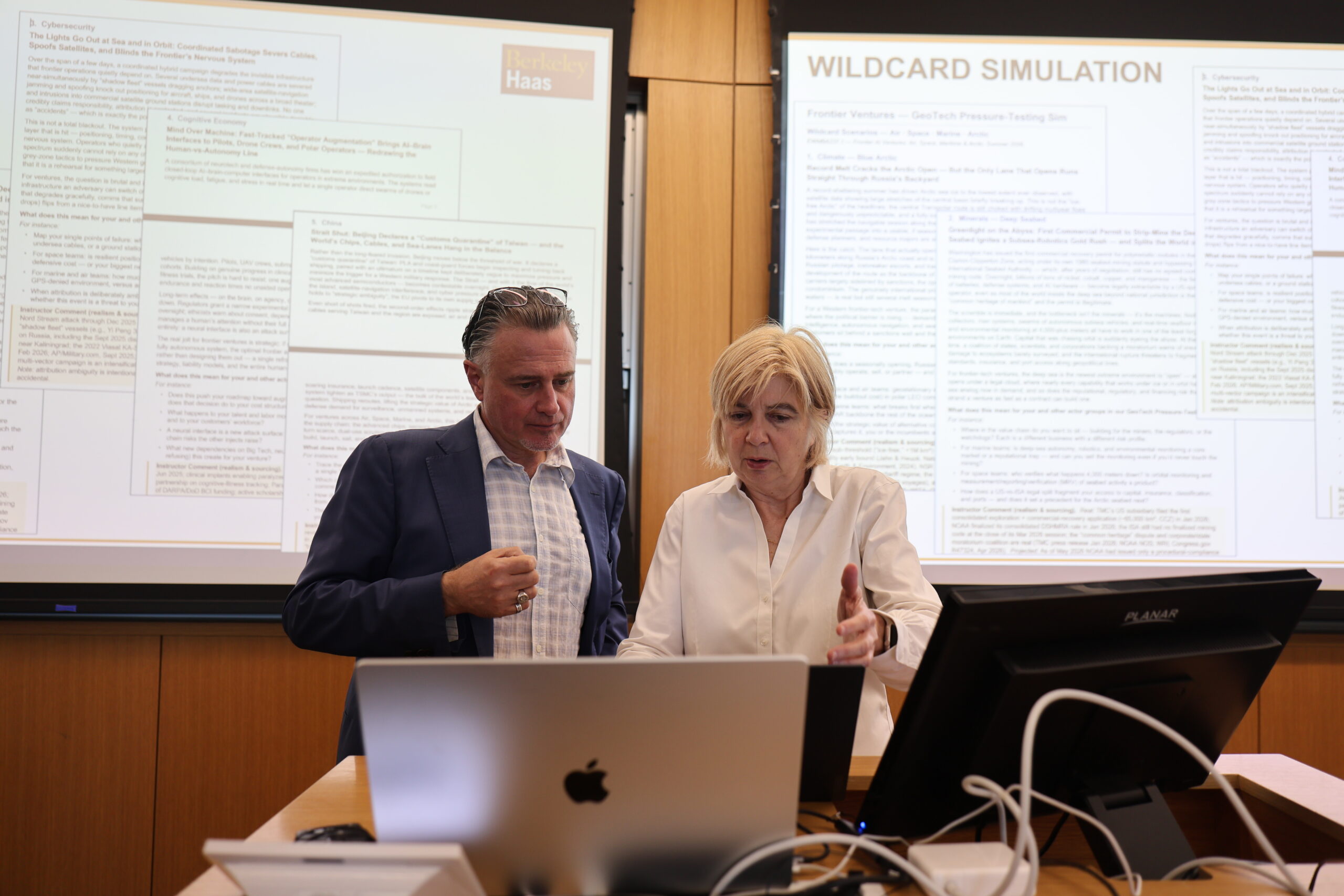 a man and a woman talking while looking at a laptop in class