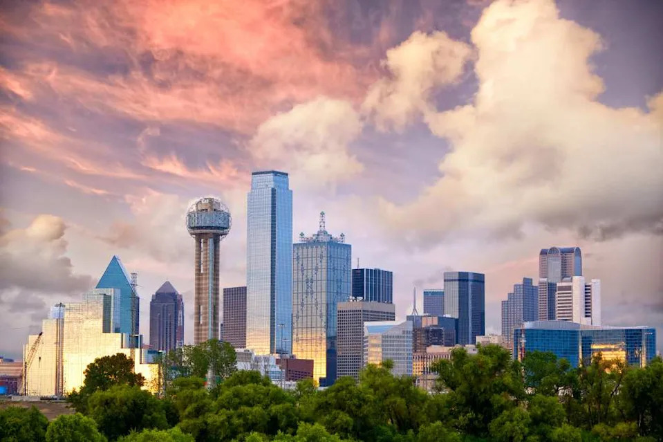 Dallas skyline at sunset with a mix of modern skyscrapers and older buildings, and Reunion Tower on the left. VisitDallas