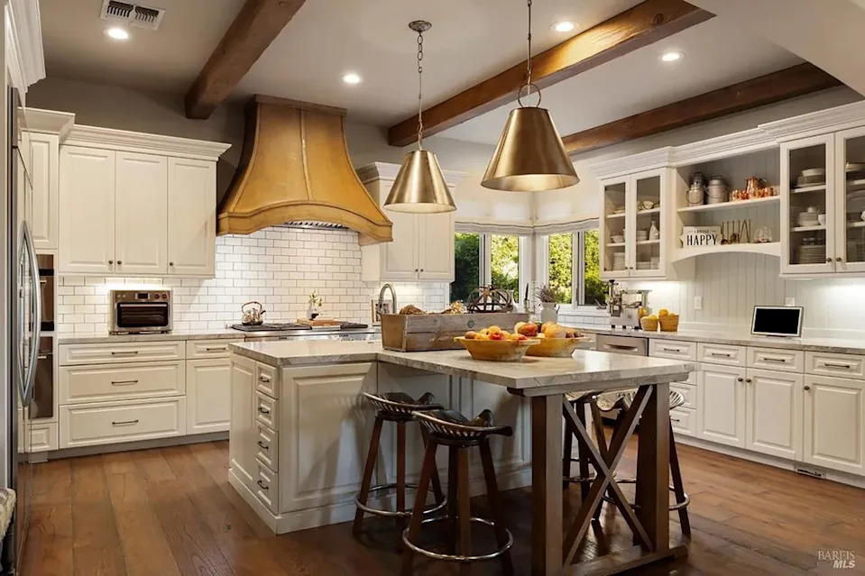 Gourmet kitchen with white cabinetry, a large central island, and exposed wood ceiling beams