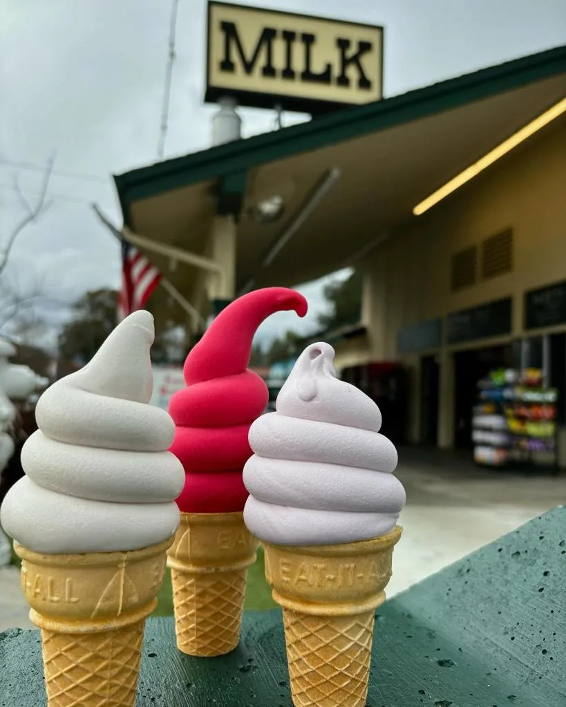 Three soft-serve ice cream cones in white, red, and pink colors in front of a “MILK” sign. Instagram/@meadowlarkdairy