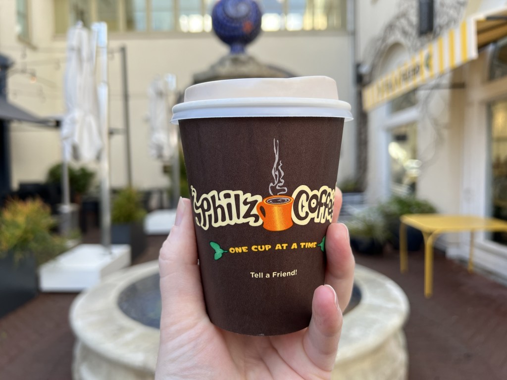 A person's hand holding a Philz Coffee cup.