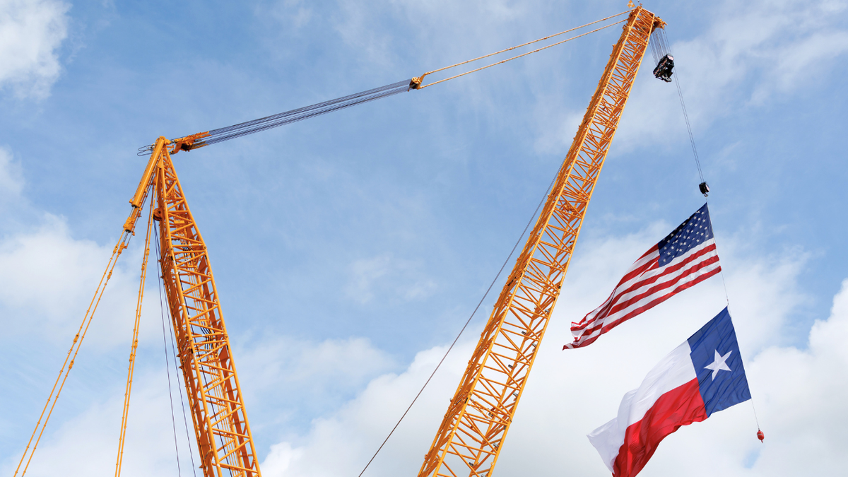 A U.S. flag and Texas state flag on a crane during a ground breaking ceremony at a future site manufacturing site.