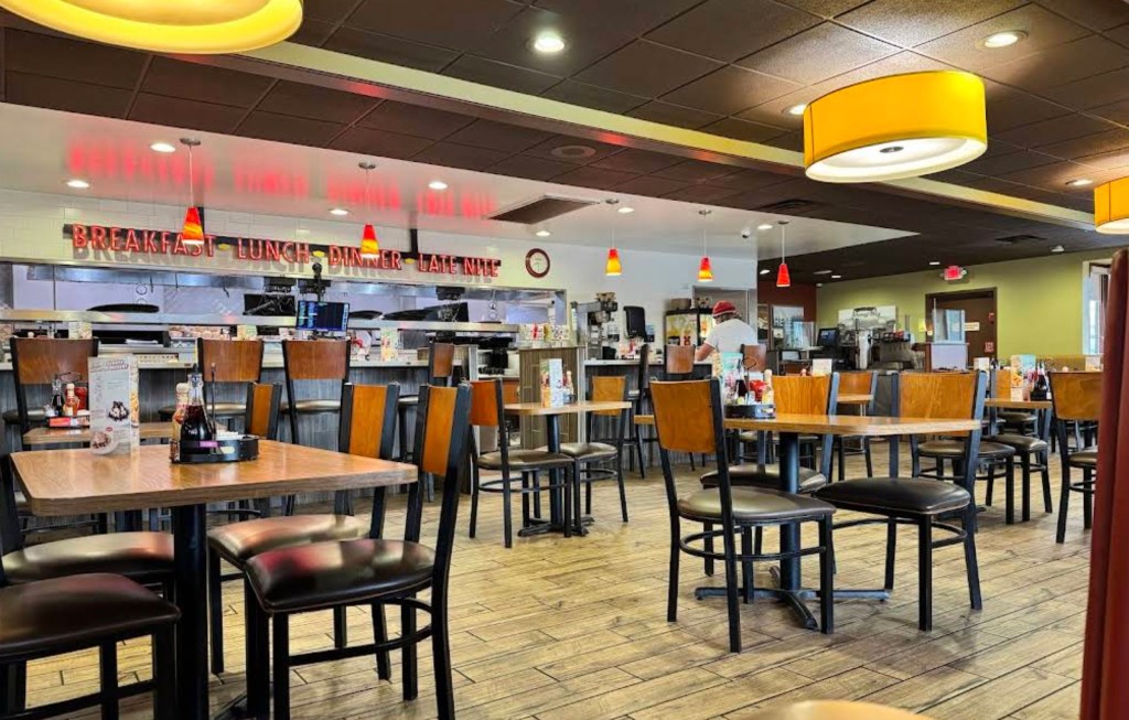 Interior of a Denny's restaurant in San Diego with tables and chairs, and a red neon sign reading "Breakfast, Lunch, Dinner, Late Nite".