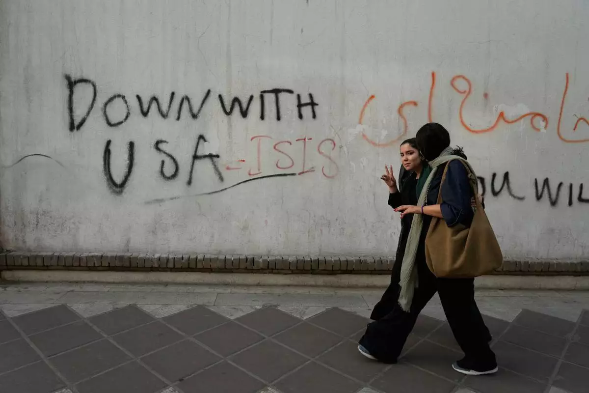 A woman reacts to the camera as she walks past an anti-U.S. graffiti painted on the wall of the British Embassy in Tehran, Iran, Saturday, June 6, 2026. (AP Photo/Vahid Salemi)
