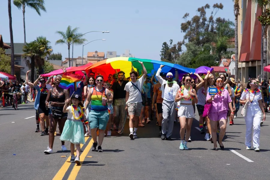 People walk under a large Pride Flag during the San Diego Pride Parade on Saturday, July 16, 2022. (Courtesy of San Diego Pride)