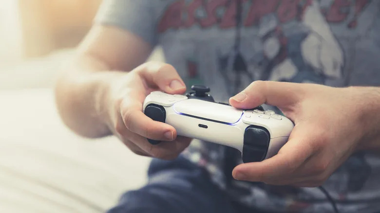 An individual holding a white Dual Sense controller between their hands, the image is cropped to just focus on the controller