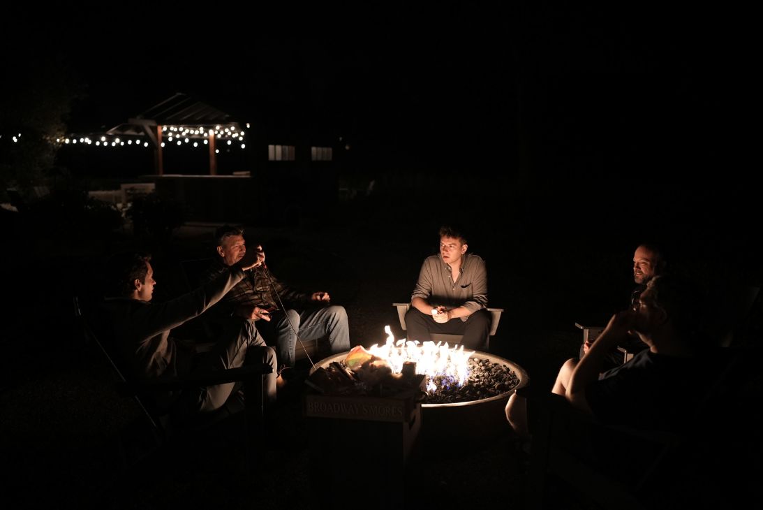 The participants speak around a firepit while eating s'mores.