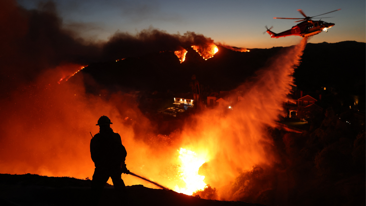 Fire personnel responding to homes destroyed as a helicopter drops water in Pacific Palisades California