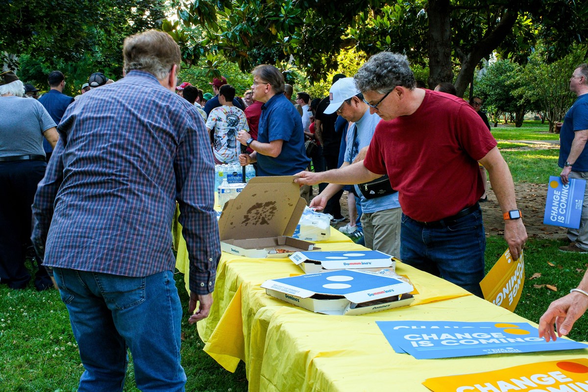 A supporter looks through a pizza box at the rally on June 4th, 2026. Hilton continued to speak to the crowd gathered around him. The event consisted of supporters both young and old. The event provided free pizza and water to the crowd.